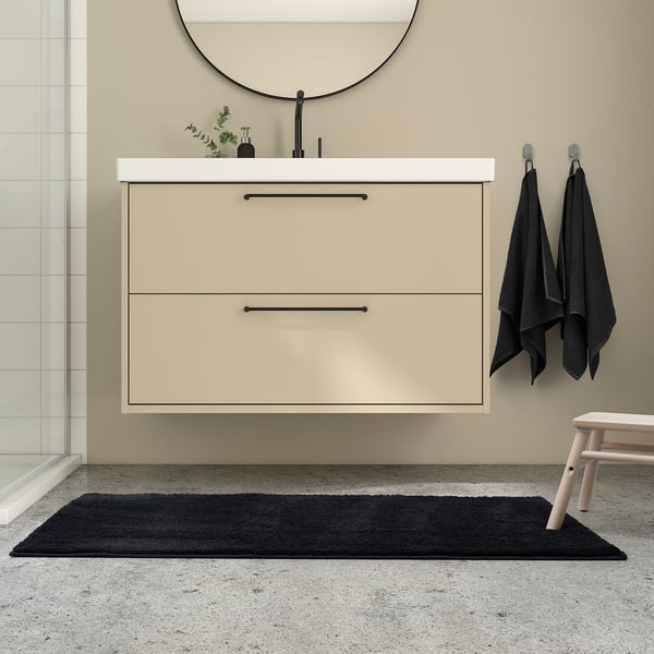 Modern bathroom with light beige BACKMÅRA mat, black towels, and floating vanity.