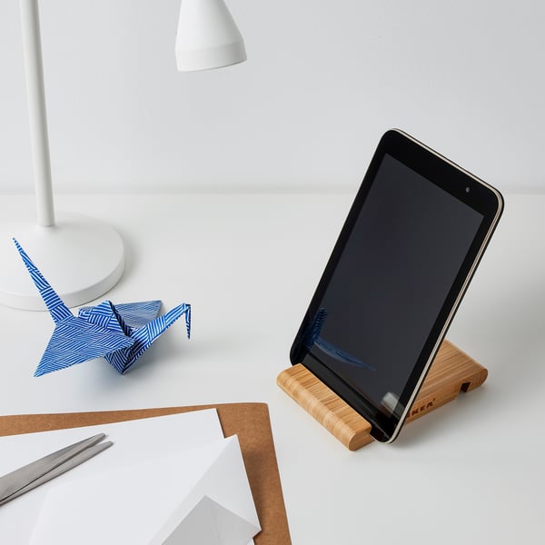 Tablet stand holds device upright next to desk lamp and paper crane on a desk.