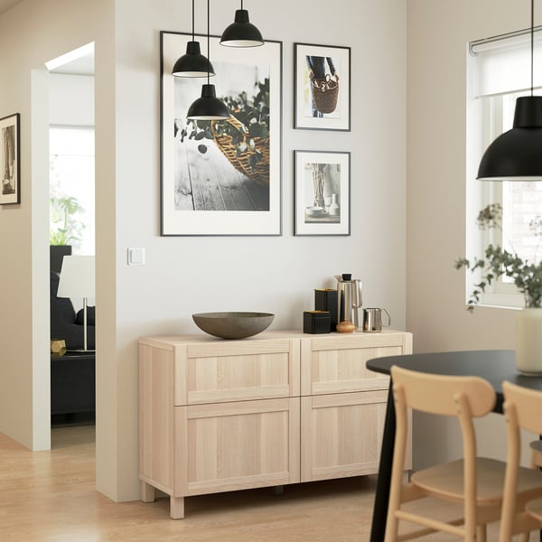 Wood sideboard with shelves, drawers & decor against white wall with art & lights.