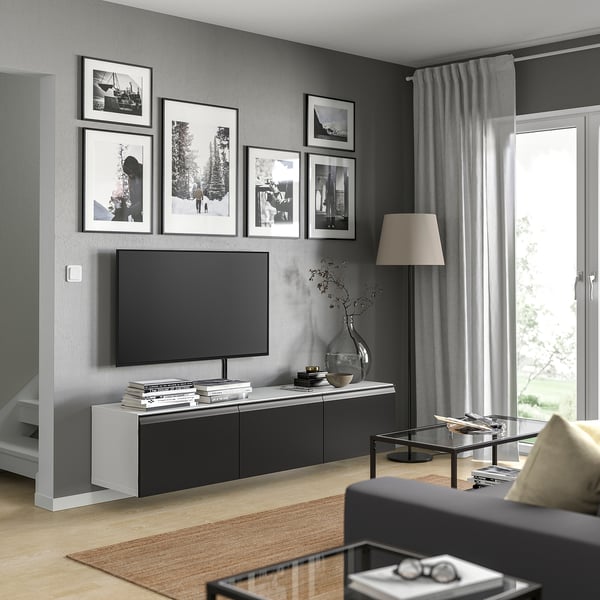 Modern living room with grey BESTÅ tv bench, black flat screen, framed photos, grey curtains, wooden floor.