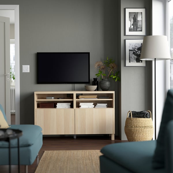 Modern living room with grey walls, featuring a BESTÅ tv bench, a large tv, blue chairs, and a cosy rug.