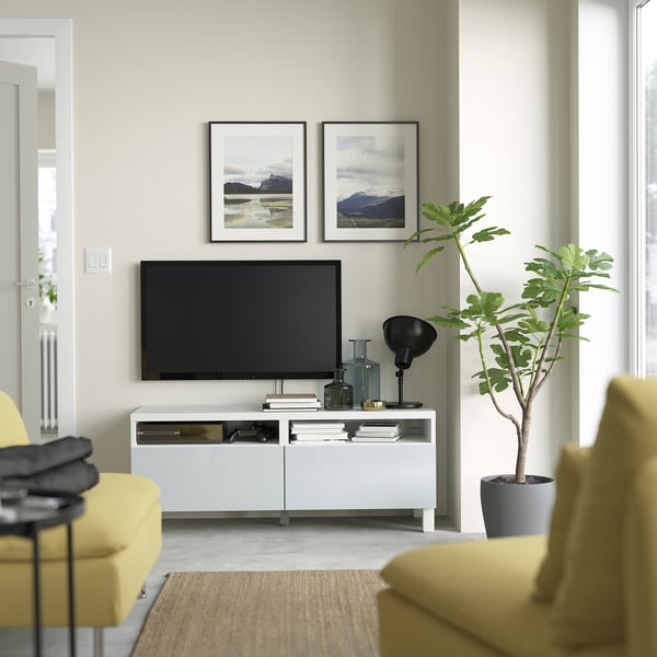 Modern living room with BESTÅ white tv stand, yellow couch, large screen tv, potted plant, framed landscapes, and clean decor.