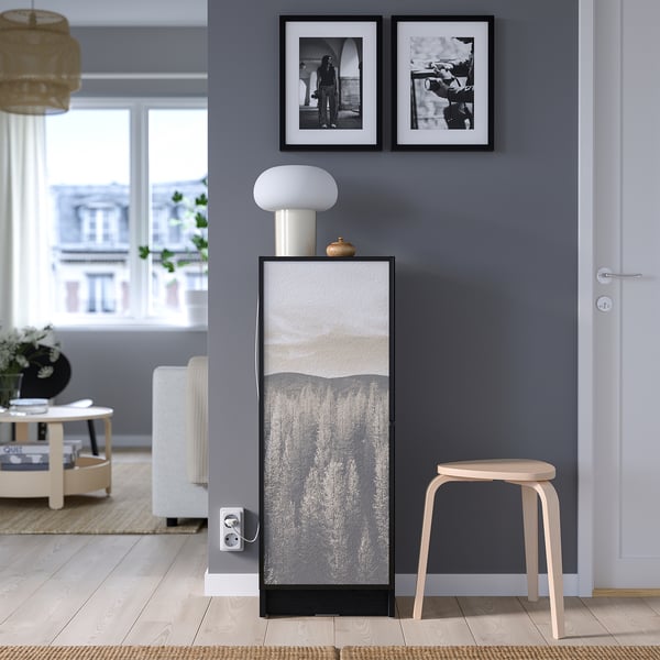 Modern living room with grey BILLY bookcase, lamp, stool, and black & white photos.