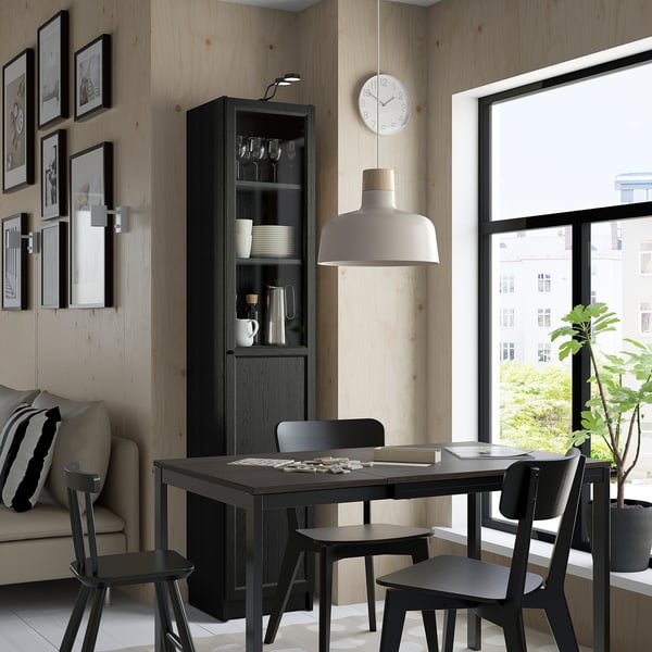 Minimalist dining space with BILLY bookcase, dark wood table, chairs, clock, and plants.