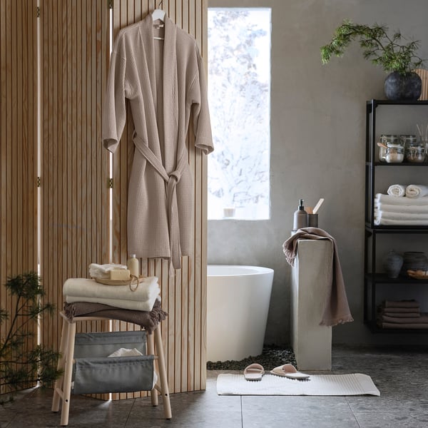 Cosy bathroom with beige bathrobe, towels, bathtub, and rug.
