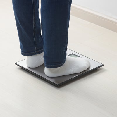 Person standing on BORSÅN scale, measuring weight on wooden floor.