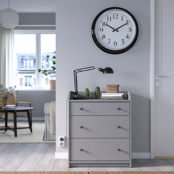 Modern grey chest with clock, lamp, basket, and plants.