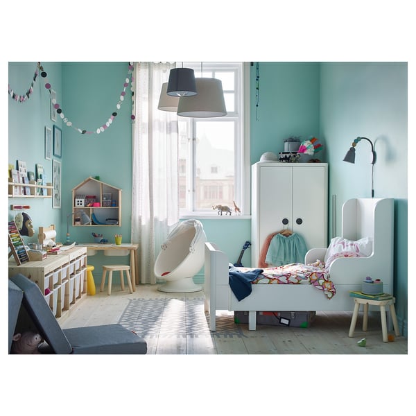Childs bedroom with white BUSUNGE extendable bed, wooden desk, hanging decorations, and blue-green walls.