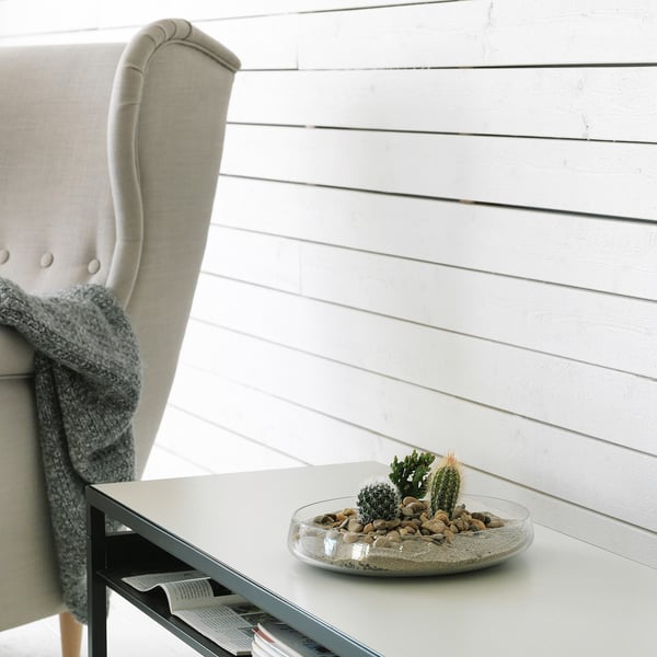 Modern living room with light grey chair, white shiplap wall, white table, and glass bowl with cacti.