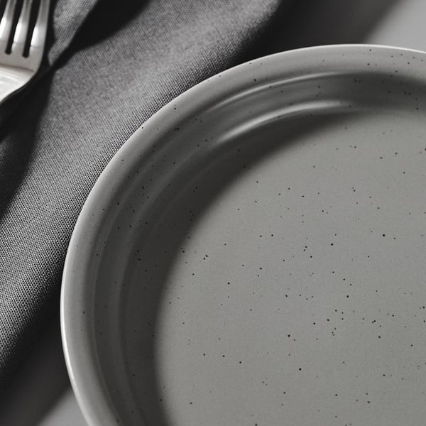 Black and white close-up of a textured, speckled stoneware plate on a grey cloth, showcasing its rustic, artisanal quality.
