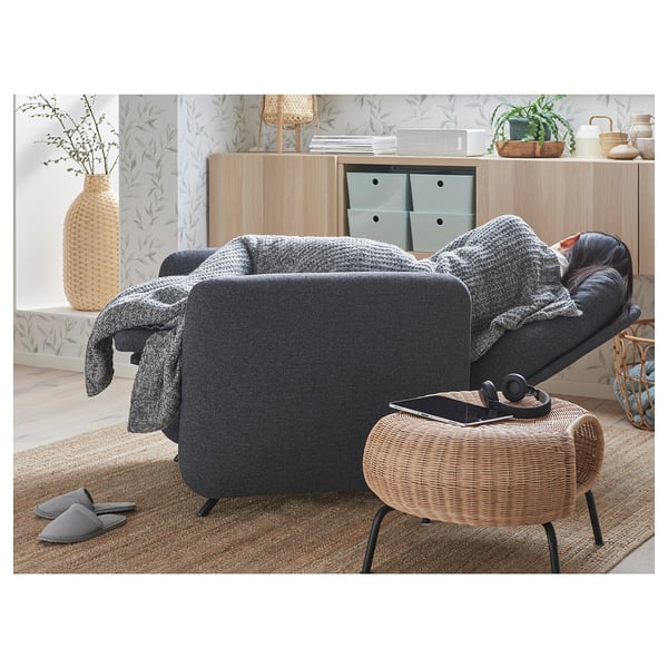 Cosy living room with dark grey EKOLSUND recliner, wicker stool, and wooden cabinet with plants.