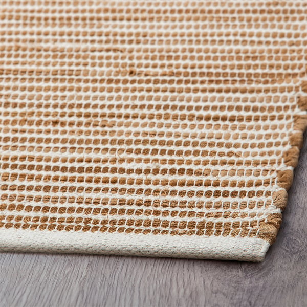 Close-up of beige, handwoven cotton rug with intricate diamond patterns, soft texture.