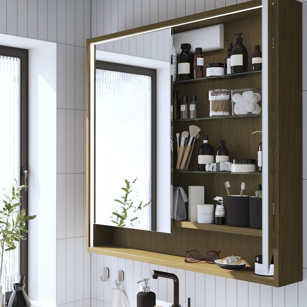 Well-organized bathroom mirror cabinet with wooden finish and integrated lighting, displaying toiletries and beauty items.