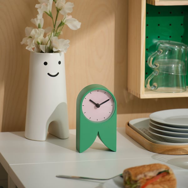 Green FLODKRÄFTA clock on white countertop with vase & sandwich.