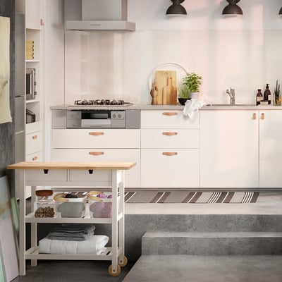 Modern kitchen with white cabinetry, black countertop and stainless steel appliances. Central island on wheels made of birch wood.