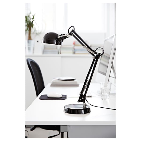 Black adjustable desk lamp on a white desk beside a computer monitor and glass.