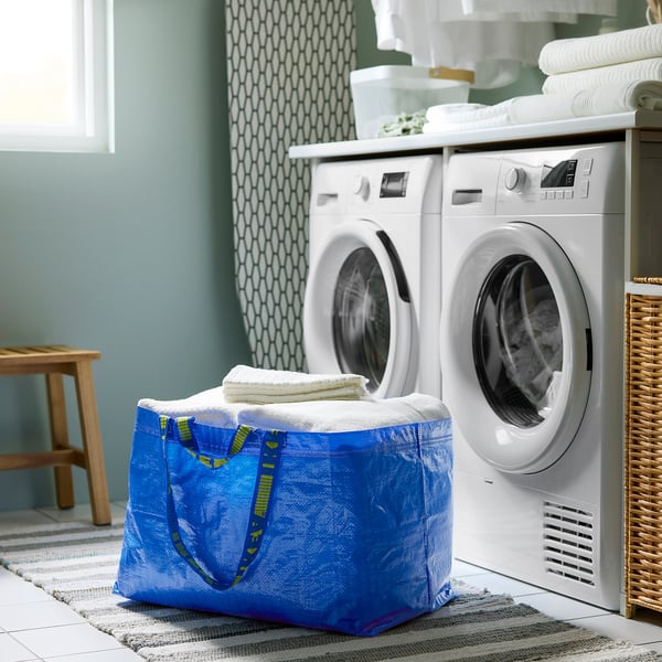 A laundry room with a blue folded FRAKTA bag holding towels. Two washing machines and folded towels on top.