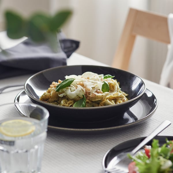 Dark bowl on plate with food, glass, and cutlery. Simple, elegant table setting.