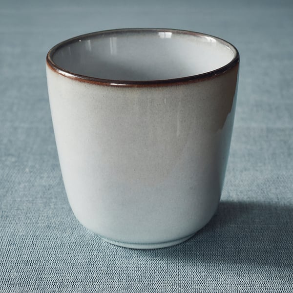 White mug with brown rim on blue surface.