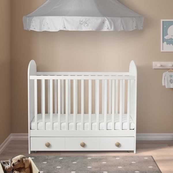 White wooden crib with curved sides, canopy, and spacious drawer, larger than nearby rug and framed art.