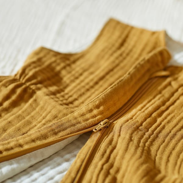 Close-up of a mustard-colored sleep bag with a visible full-length zip, showcasing its soft, textured fabric.