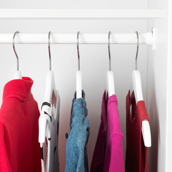 Closet with colourful kids clothes on white hangers.