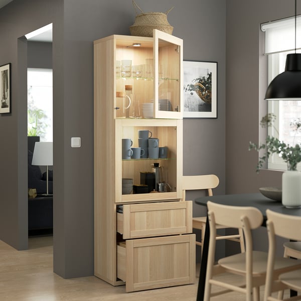 Glass-door cabinet with cups, kitchenware, drawers, and plant. Modern dining area.