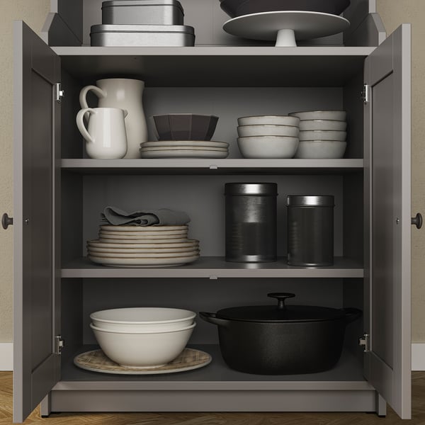 Open grey HAUGA kitchen cabinet with black, white, and metal dishes, cookware, and utensils.