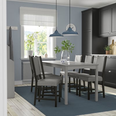 Modern kitchen with grey HAUGA dining set, cushioned chairs, blue lights, window, dark cabinets, and rug.