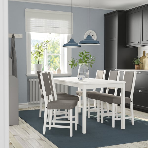 Modern white HAUGA dining set with 6 grey upholstered chairs in cosy kitchen, surrounded by black cabinets and wood floors.
