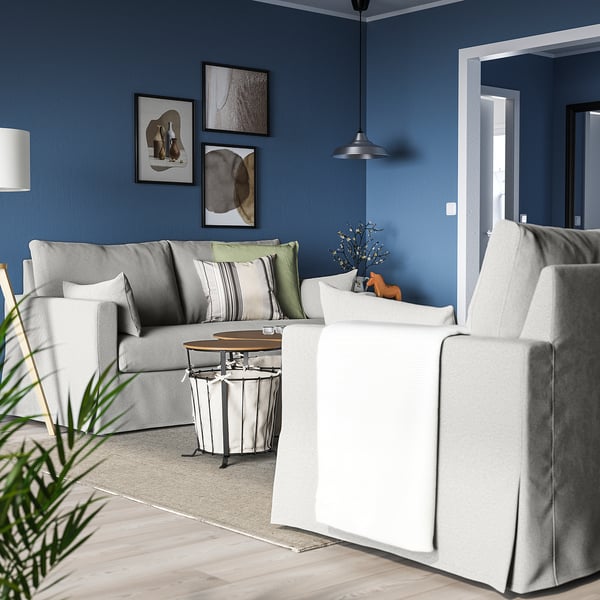 Cosy blue living room with HYLTARP grey sofa, white coffee table, hanging light, art, and plant.