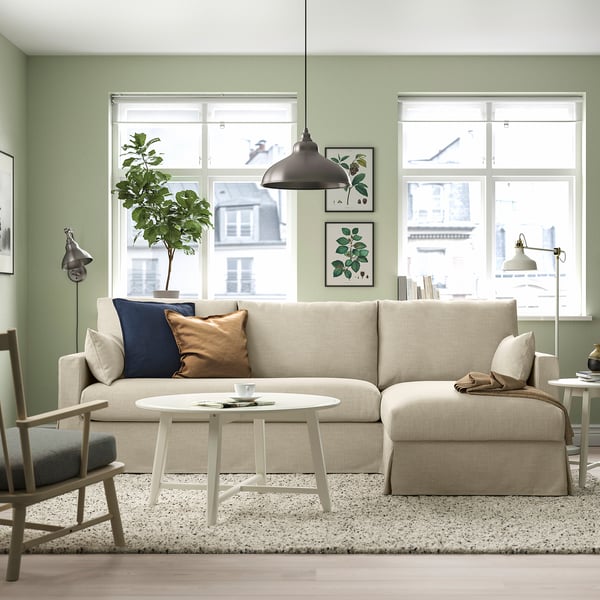 Cosy living room with beige HYLTARP sofa, cushions, green wall, coffee table, plant, lamp, two windows.