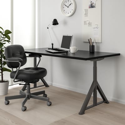 IDÅSEN desk & chair setup with cable net, laptop, mug & lamp. Whiteboard & clock in background.