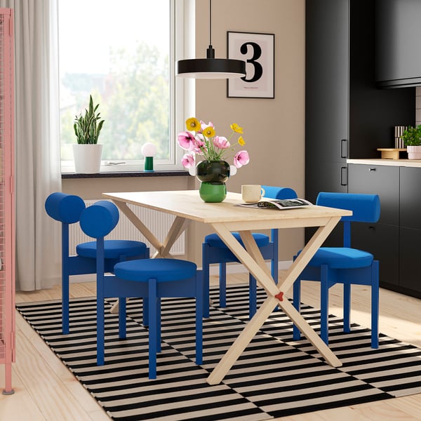 IKEA PS 2026: light wood table, blue chairs; modern, airy dining setup.