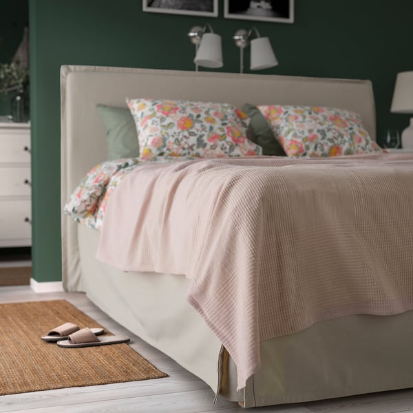 Pink recycled cotton INDIRA bedspread on a double bed, with pastel pillows, slippers, and rug.