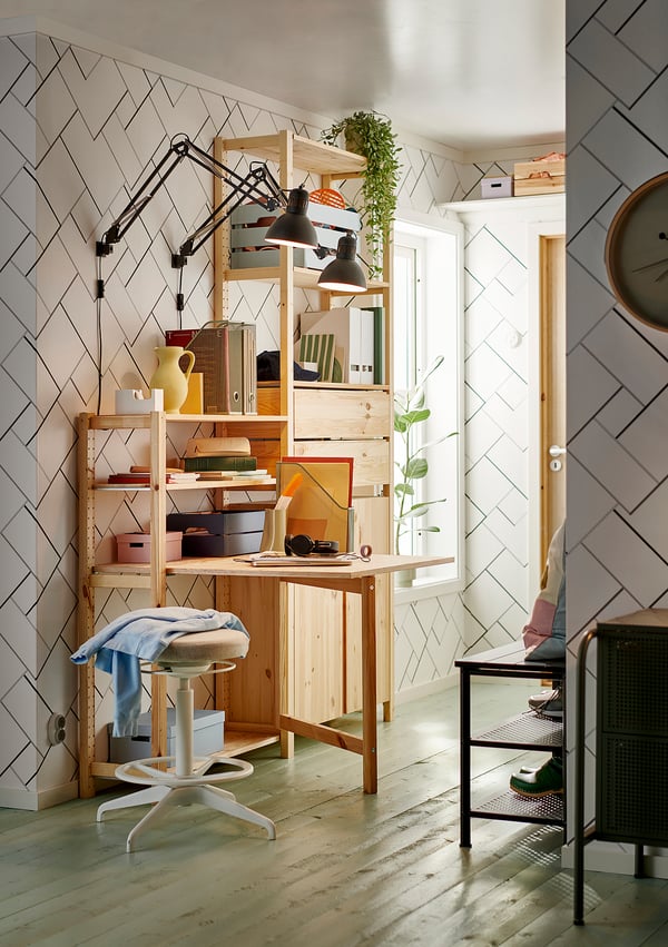 Home office with IVAR pine desk and shelves, black lamp, white stool, books, and decor.