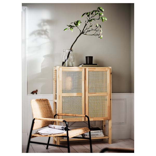 Modern living room corner with light-colored wooden IVAR storage, woven bamboo doors, and black metal chair against a beige wall.