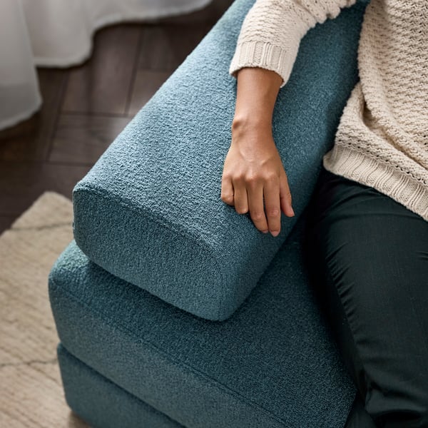 Person resting arm on teal JÄTTEBO sofa, knit sweater visible.