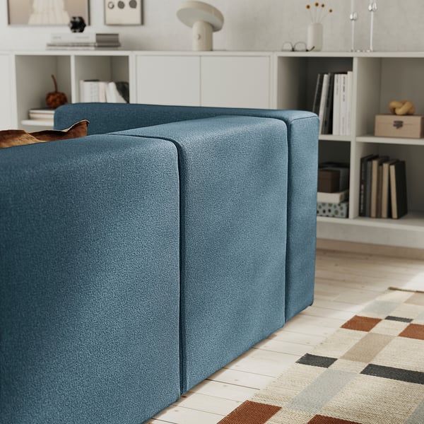 Blue sectional sofa with storage, bookshelves, and rug.