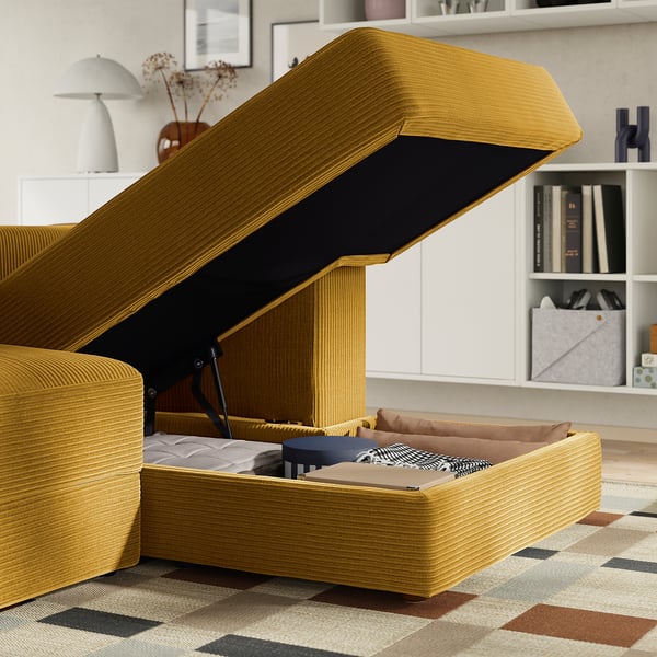 Mustard sofa with storage. Bed inside, opened for use. Bookshelf and lamp behind.