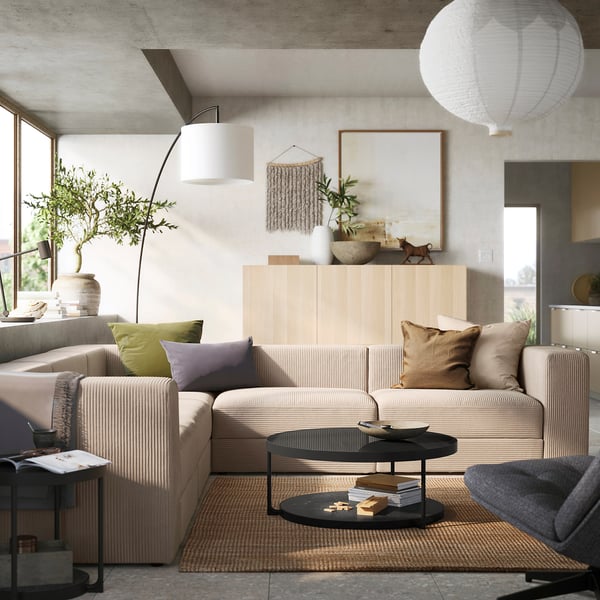 Modern living room a light beige JÄTTEBO modular sofa with colourful pillows, a wooden cabinet with decor, and a black coffee table on a woven rug.