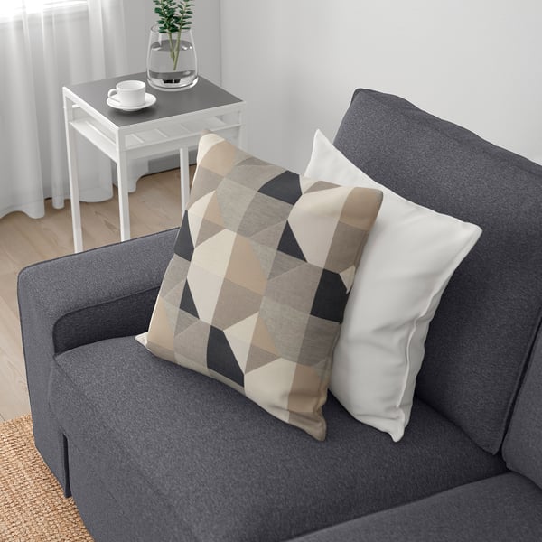 Grey sofa with removable cushions, one patterned, near side table with plant and cup.