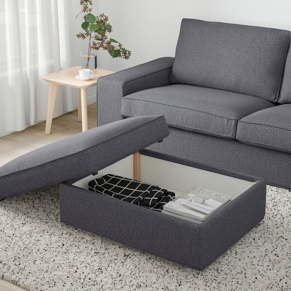 Modern living room with grey KIVIK footstool, couch, and side table holding plant and cup.