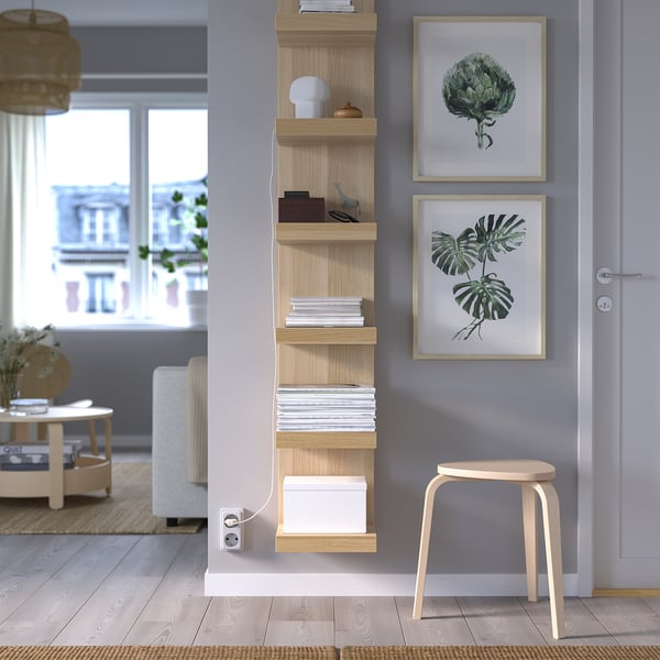 Blue wall with LACK shelf, magazines, box, lamp, plant prints, stool. Minimalist, well-lit room.