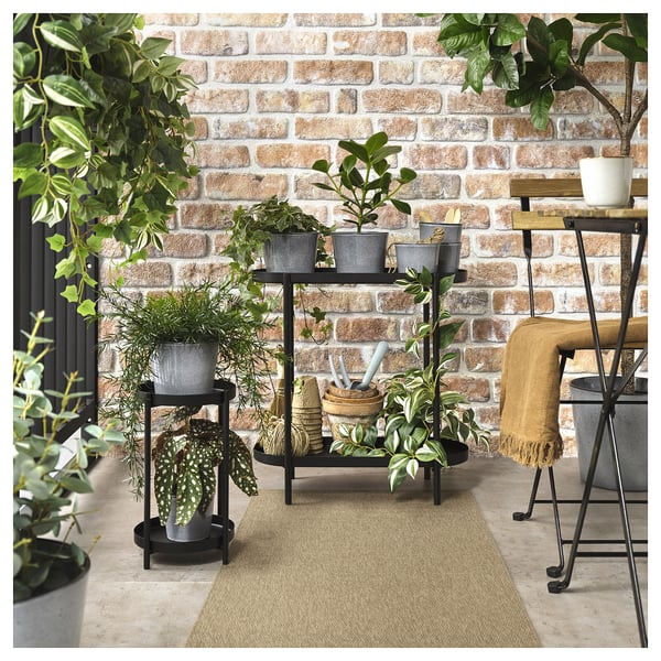 A beige flatwoven LÄTTBETONG rug placed outside against a brick wall with potted plants and furniture.