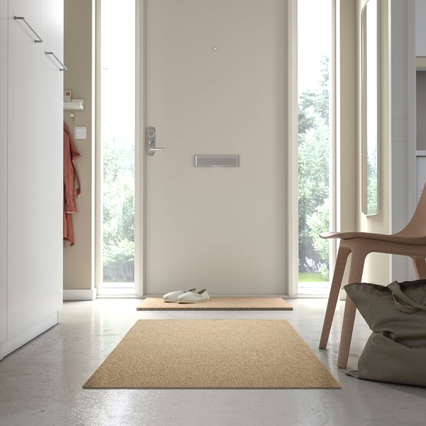 Beige LÄTTBETONG rug in hallway, near door and chair, complements minimalist decor.