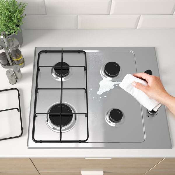 Hand cleaning a gas hob with 4 burners and electronic ignition.