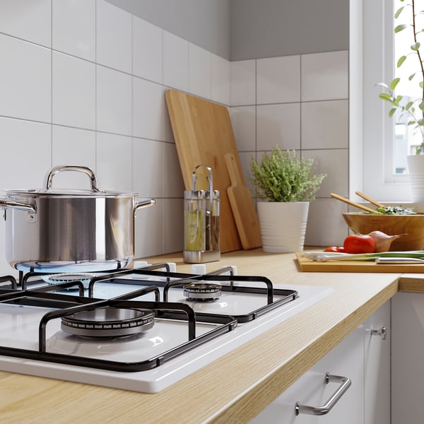Modern kitchen with gas stove, pots, wooden utensils, and plants.