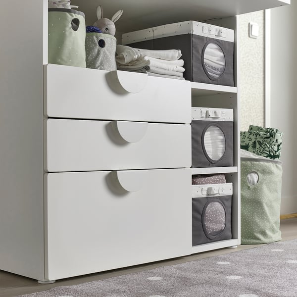 White storage unit with drawers, grey boxes with mesh windows, and a cuddly toy. Used for organising baby items.