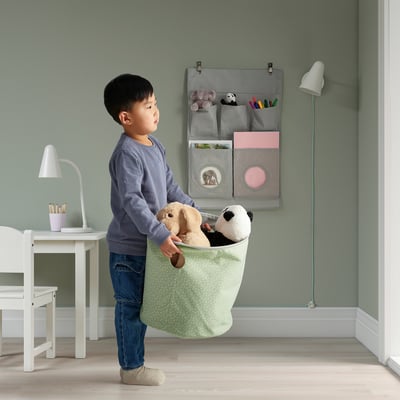 Young boy holding reversible toy bag, which stands upright and organises stuffed animals, with pastel polka dots pattern visible.